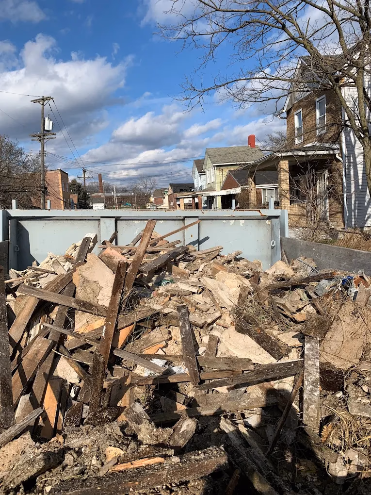 Dumpster filled with wood and debris in a residential neighborhood under a partly cloudy sky.