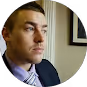 Side profile of a man with short hair wearing a suit and tie inside a room.